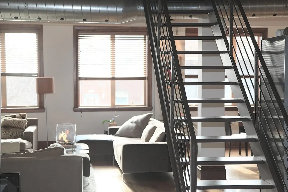 Przestronny salon w stylu loft z ceglaną ścianą, skórzaną kanapą i dużymi oknami w czarnych ramach.